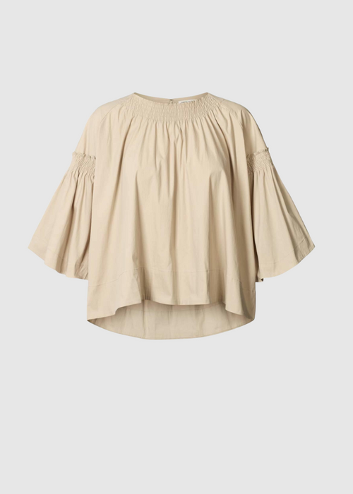A light beige blouse with a smocked round neckline, gathered elbow-length sleeves, and a high-low hemline, shown against a solid light grey background.