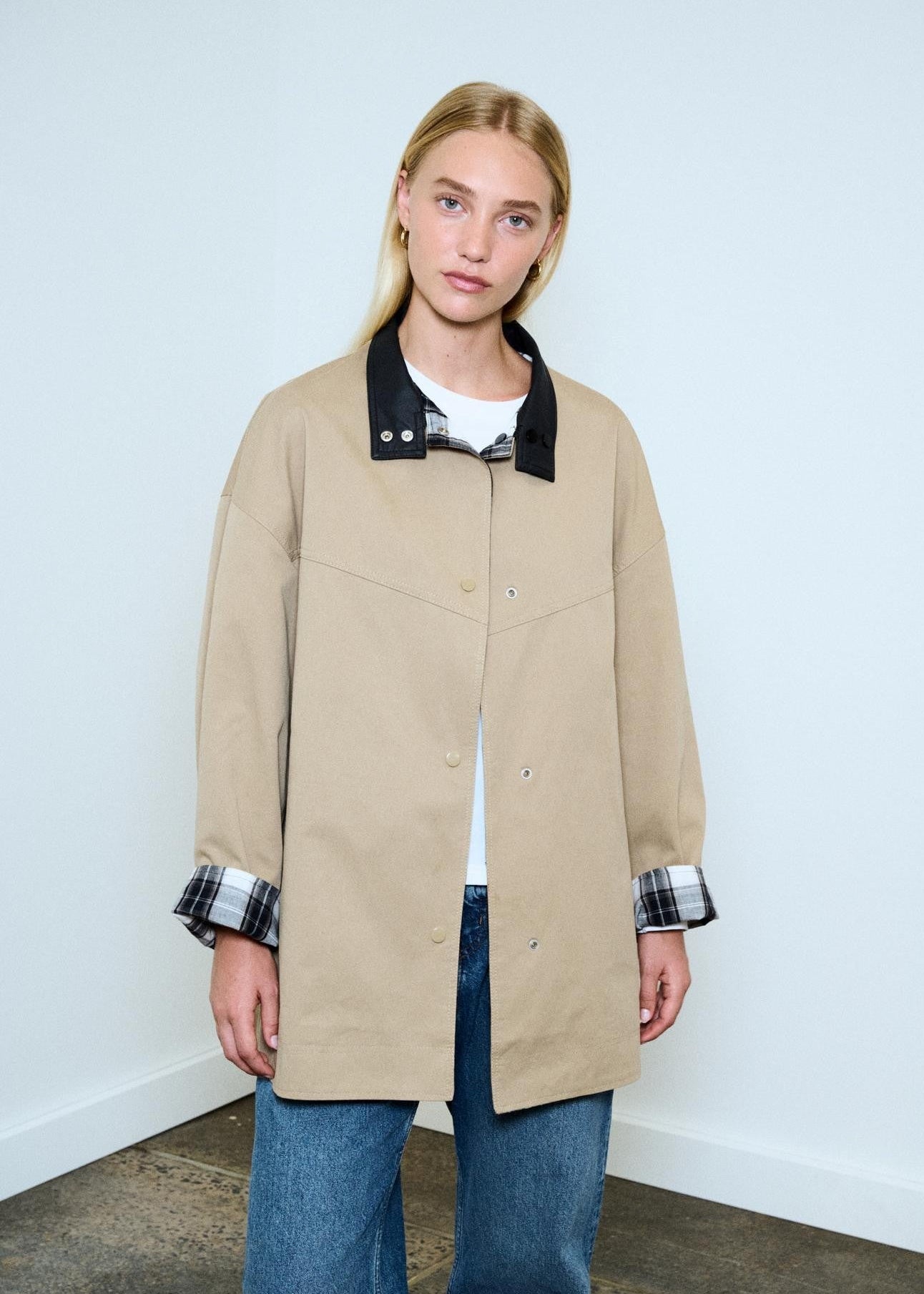 Person wearing a beige jacket with a black collar against a white background