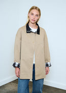 Person wearing a beige jacket with a black collar against a white background