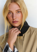 Person wearing a beige jacket with a black collar against a white background