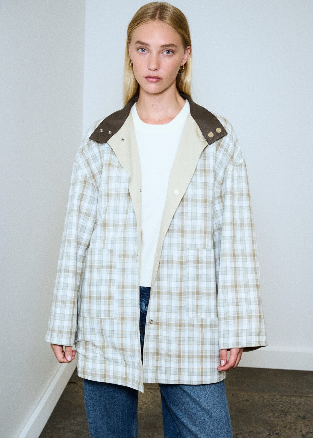 Woman wearing a plaid coat with a white shirt and jeans against a plain background