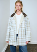 Woman wearing a plaid coat with a white shirt and jeans against a plain background