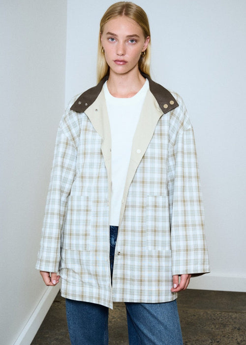 Woman wearing a plaid coat with a white shirt and jeans against a plain background