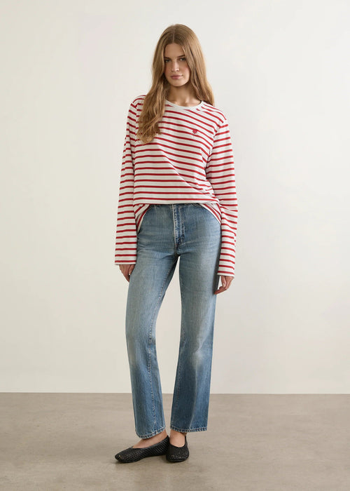 Woman wearing a red and white striped sweater and blue jeans against a plain background