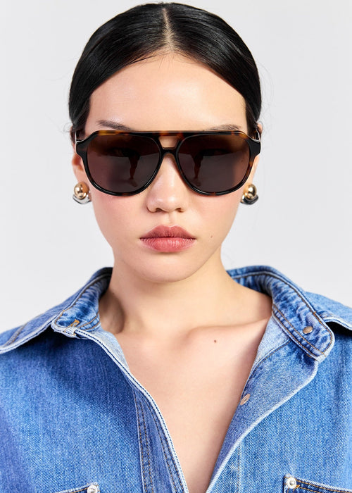 Model wearing tortoise shell sunglasses on grey background