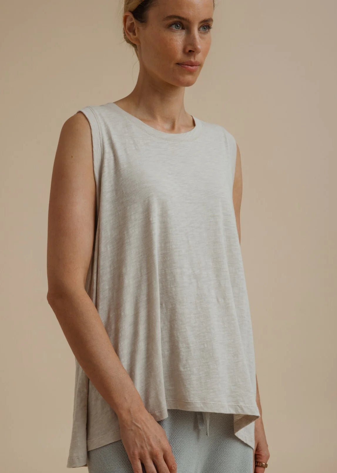 Woman wearing a light beige sleeveless top and pants on a beige background