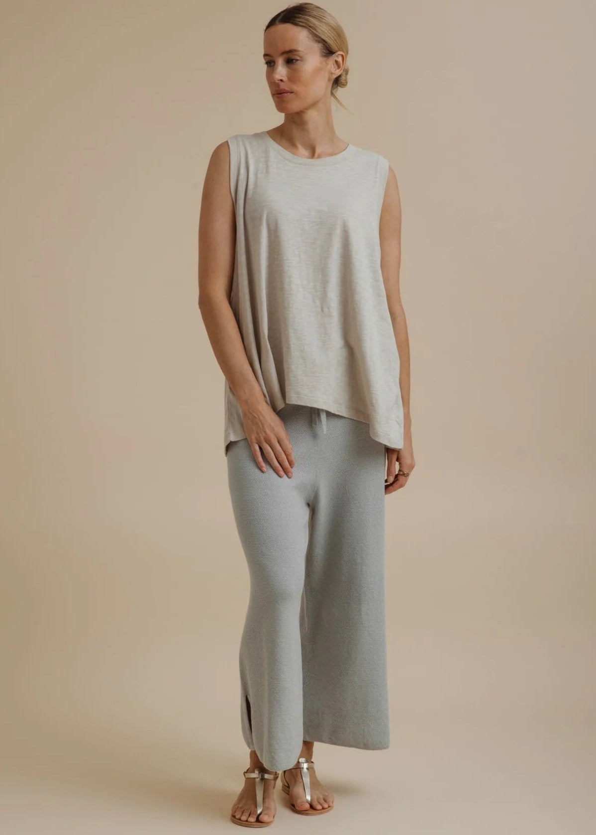 Woman wearing a light beige sleeveless top and pants on a beige background