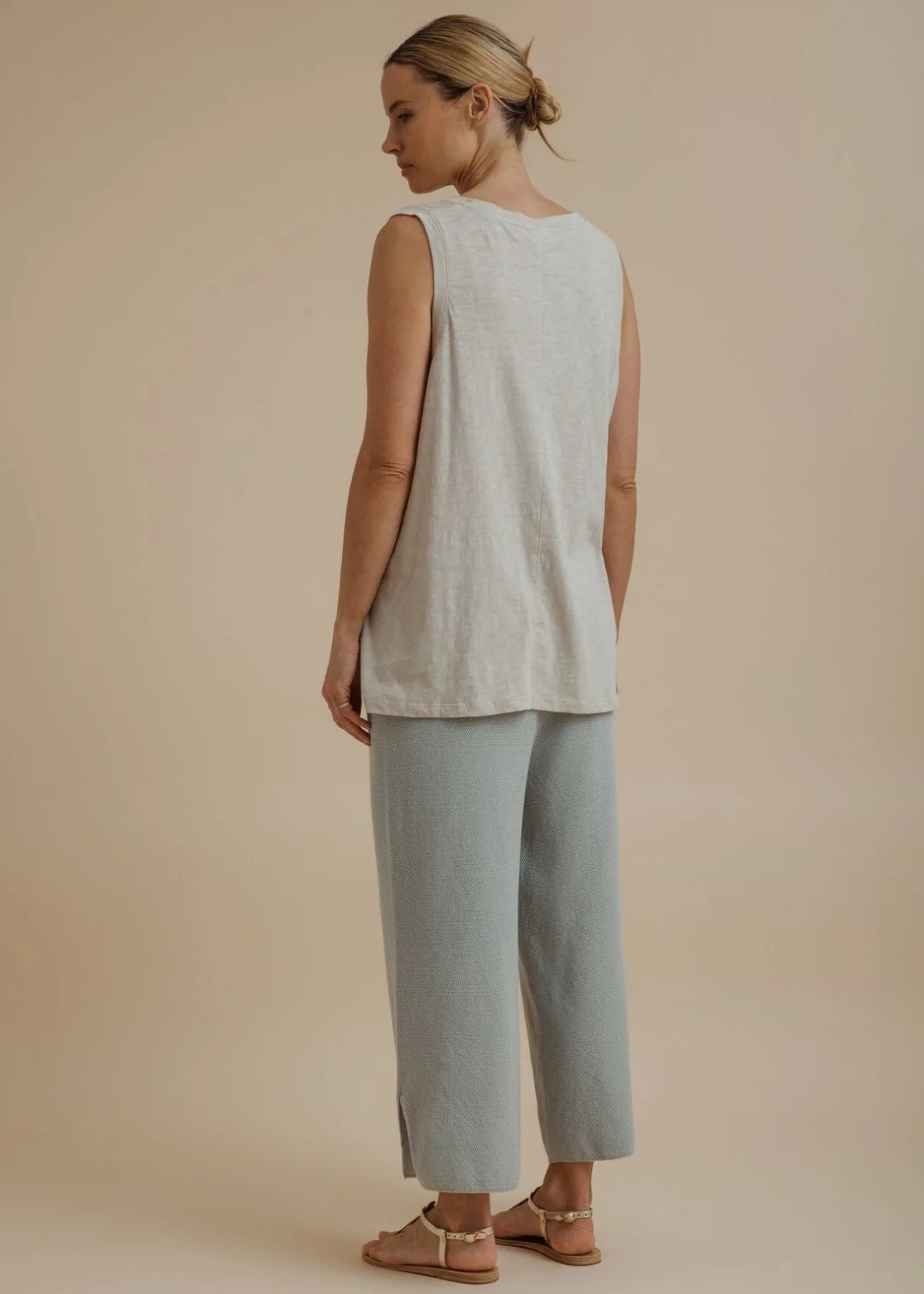 Woman wearing a light beige sleeveless top and pants on a beige background