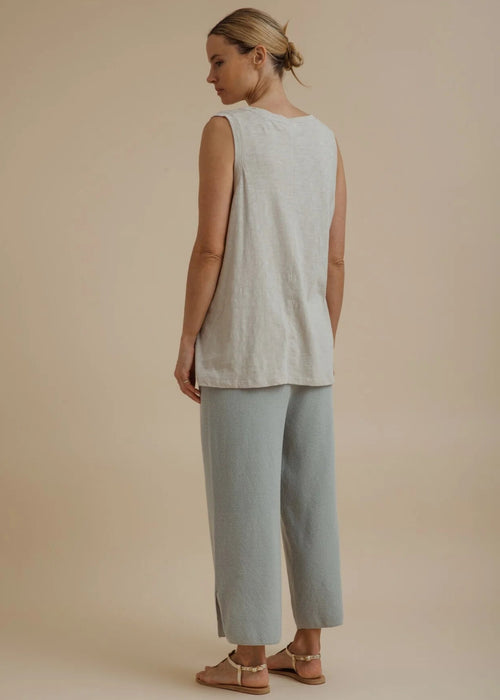 Woman wearing a light beige sleeveless top and pants on a beige background