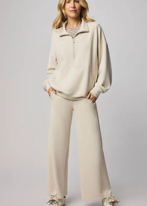 Woman wearing a beige outfit with wide-leg pants against a plain background