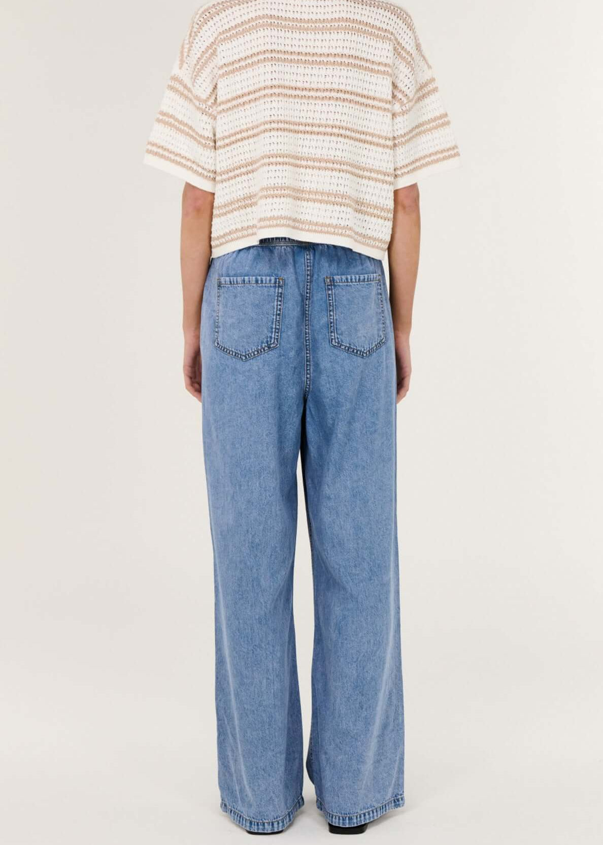 Person wearing a striped shirt and blue jeans on a white background