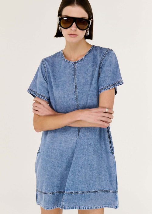 Woman wearing a blue denim dress with sunglasses on a white background