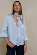 Woman wearing a light blue blouse with a bow tie against a beige background