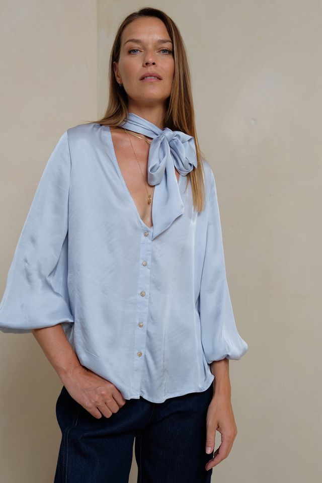 Woman wearing a light blue blouse with a bow tie against a beige background