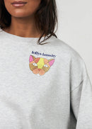 A model wearing a light grey heather crewneck sweatshirt with a colourful embroidered cat graphic and 'Jelly Jane' text on the left chest, paired with tan pants against a plain white background.