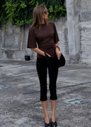Woman wearing a brown top and black pants standing in an urban setting.