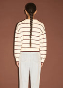 Woman wearing a striped sweater and light blue jeans against a brown background