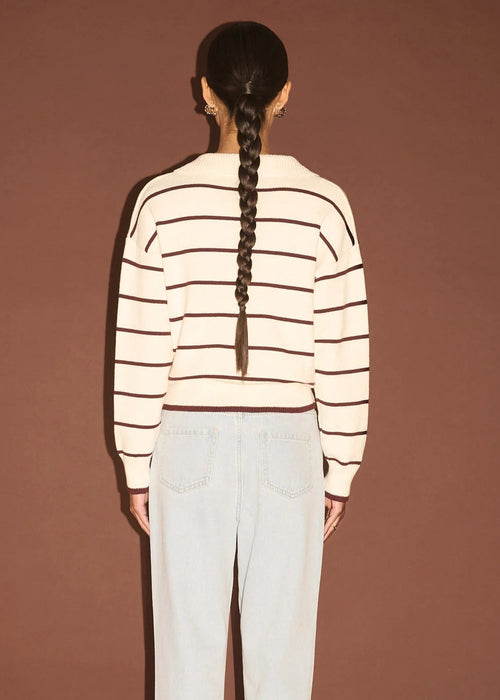 Woman wearing a striped sweater and light blue jeans against a brown background