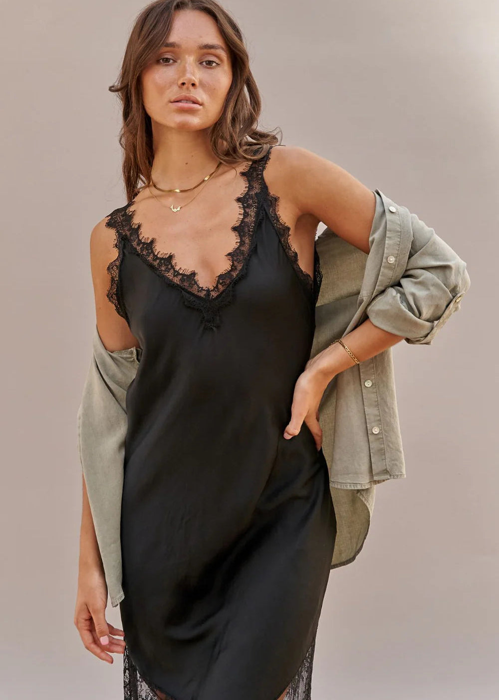Woman wearing a black slip dress with lace details on a plain background