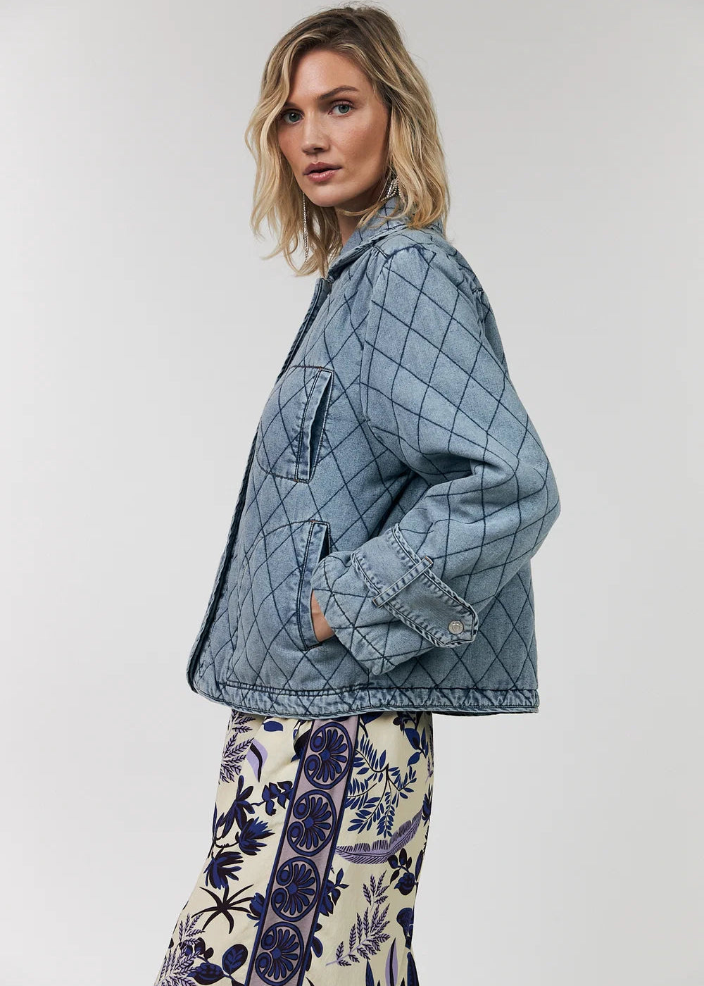 Woman wearing a blue quilted jacket and patterned pants on a white background