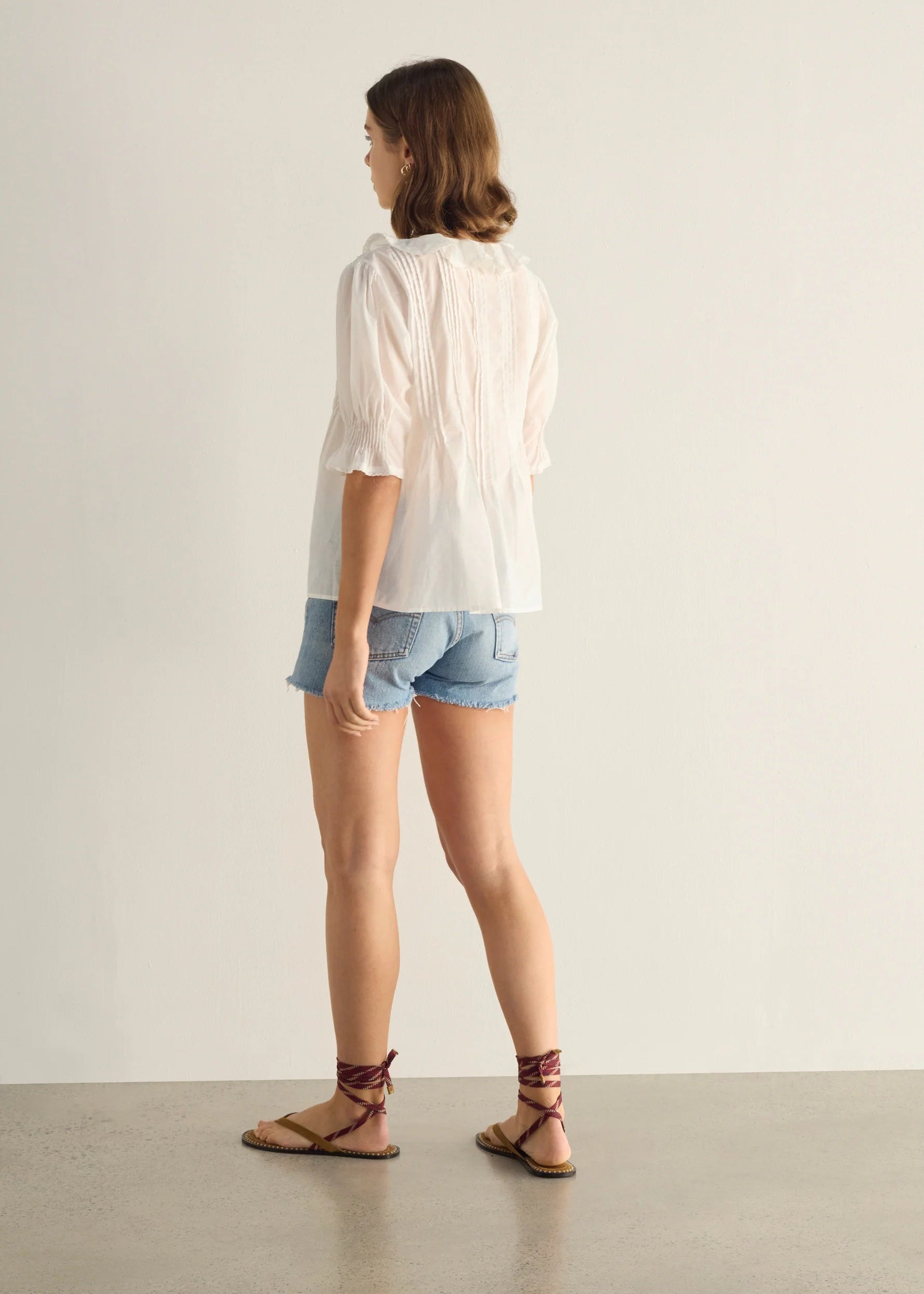 Woman wearing a white blouse and denim shorts against a plain background