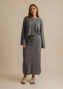 Woman wearing a grey sweater and textured skirt on a beige background