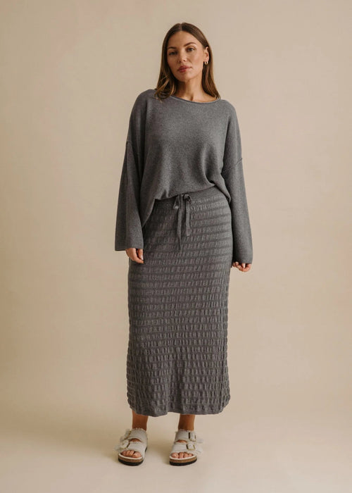 Woman wearing a grey sweater and textured skirt on a beige background