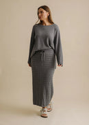 Woman wearing a grey sweater and textured skirt on a beige background