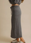 Woman wearing a grey sweater and textured skirt on a beige background