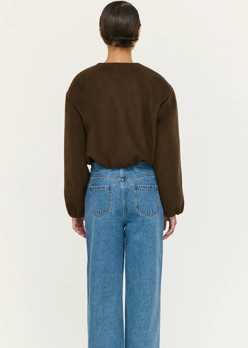 Women wearing a brown jacket, white shirt, blue jeans, and black shoes on a white background