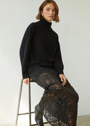 Woman wearing a black turtleneck and lace skirt against a white background