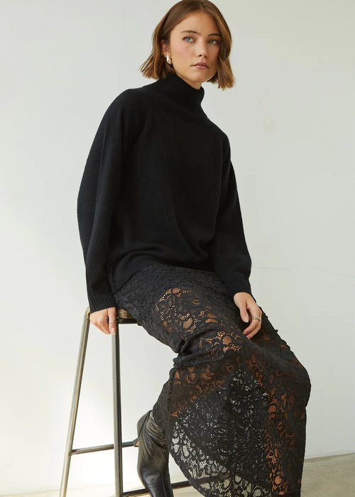 Woman wearing a black turtleneck and lace skirt against a white background