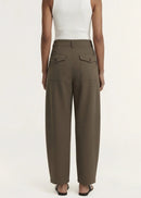 A model wearing a white sleeveless top and high-waisted, wide-leg brown trousers, paired with black flip-flops, against a plain off-white studio background.