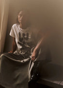 Person wearing a white t-shirt with a graphic design, sitting in a dimly lit room.