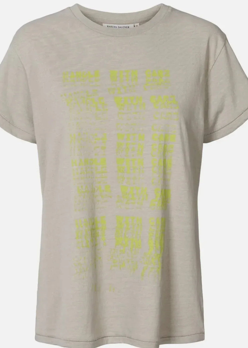 A light beige short-sleeve t-shirt with a yellow graphic print of stacked text on the front, displayed against a light grey background.