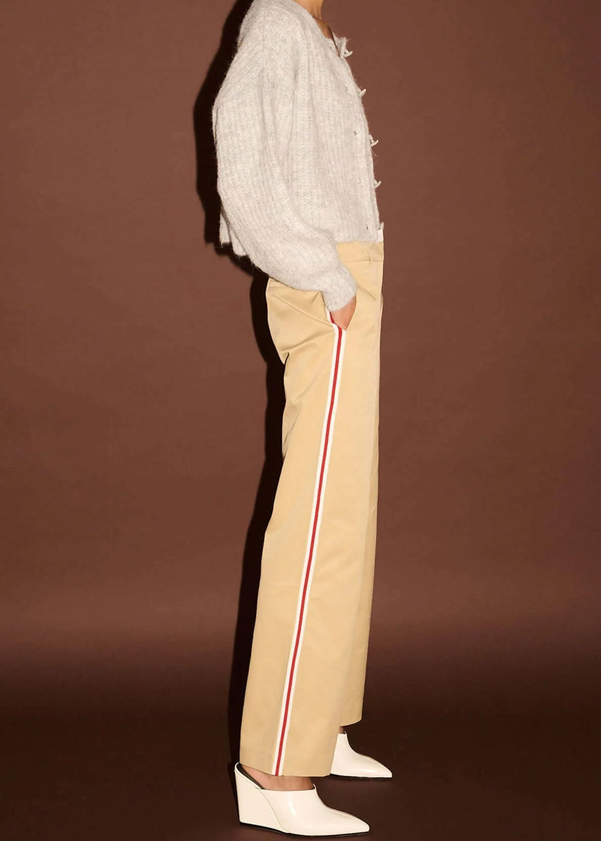 Woman wearing white top, beige pants,  on a brown background