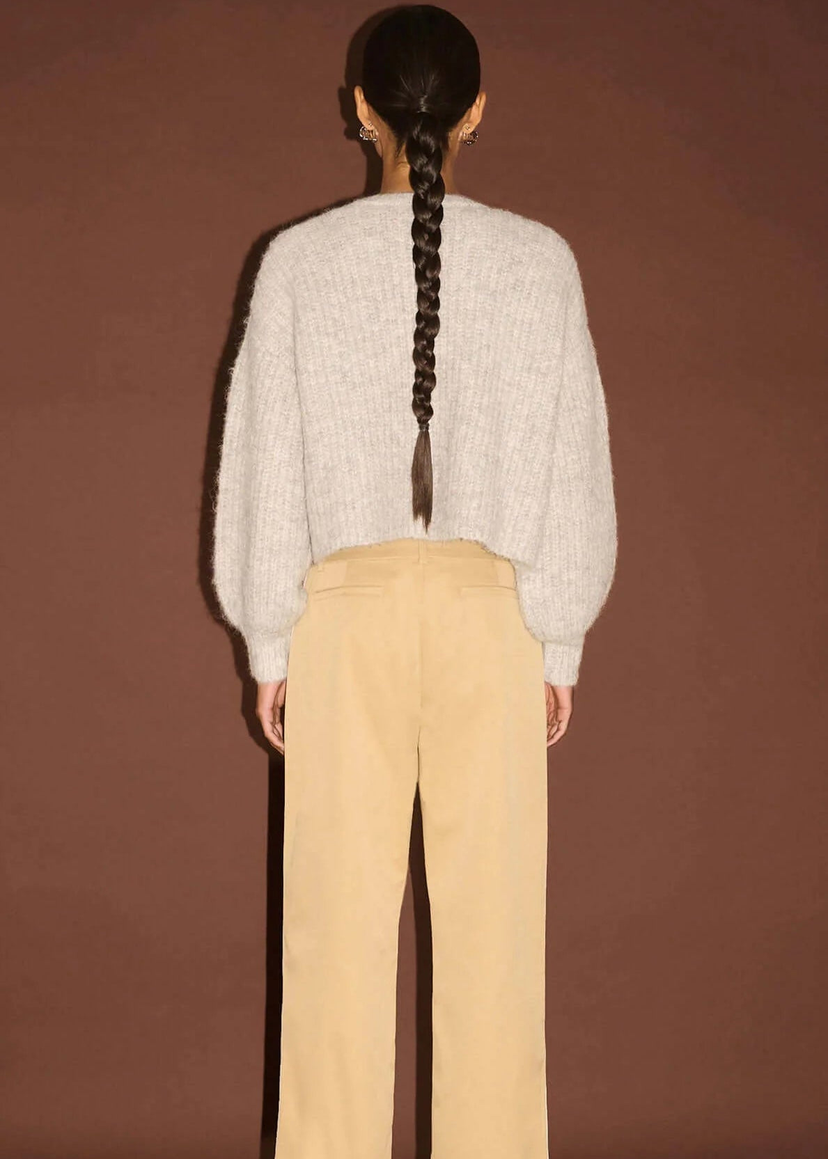 Woman wearing white top, beige pants,  on a brown background
