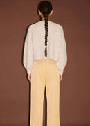 Woman wearing white top, beige pants,  on a brown background