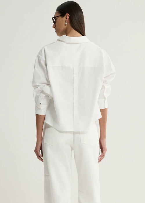 A model viewed from the back wearing a white oversized button-down shirt and matching white wide-leg trousers, paired with black sandals against a plain light background.
