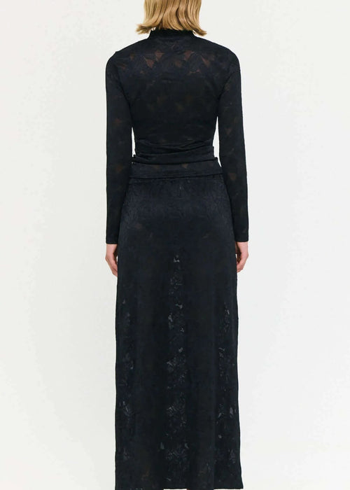 Woman wearing a black outfit with a long skirt and top on a white background