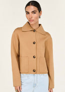 Woman wearing a tan jacket with black buttons on a white background