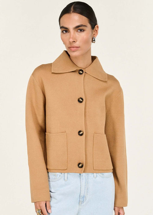 Woman wearing a tan jacket with black buttons on a white background