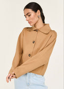 Woman wearing a tan jacket with black buttons on a white background