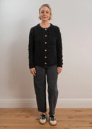 Woman wearing a black cardigan with button details on a light grey background