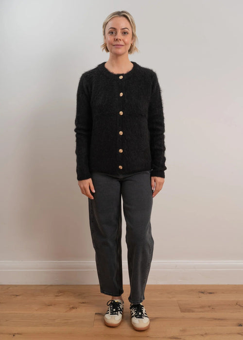 Woman wearing a black cardigan with button details on a light grey background