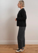 Woman wearing a black cardigan with button details on a light grey background