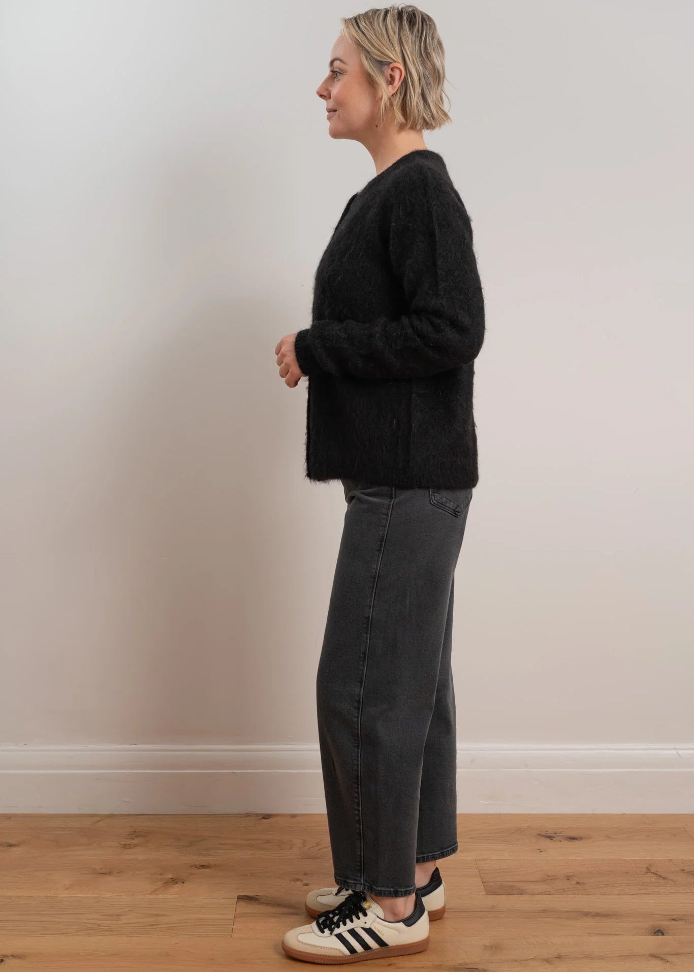 Woman wearing a black cardigan with button details on a light grey background