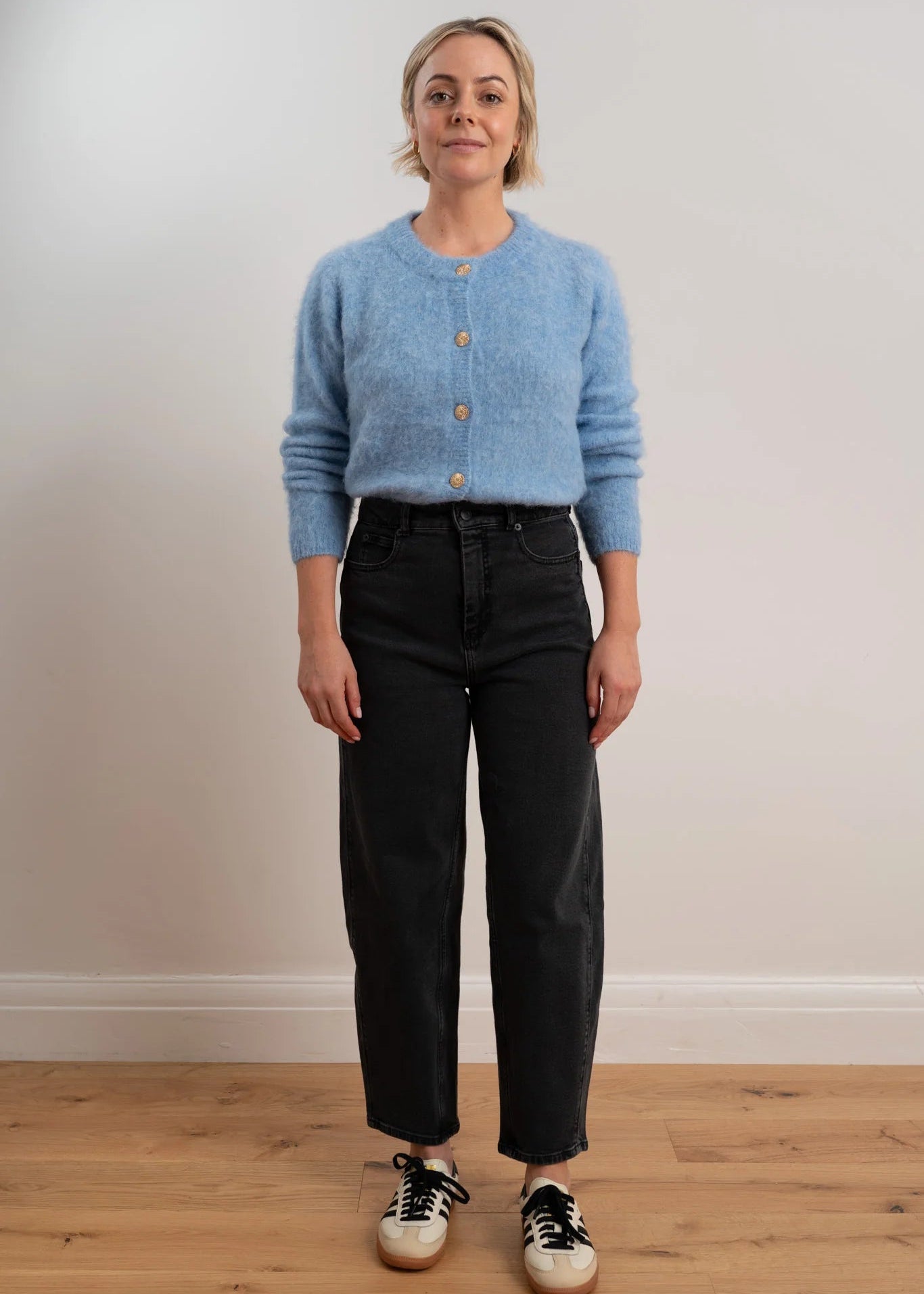 Woman wearing a light blue cardigan with buttons on a plain background