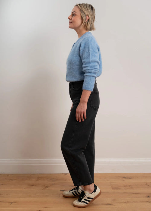 Woman wearing a light blue cardigan with buttons on a plain background