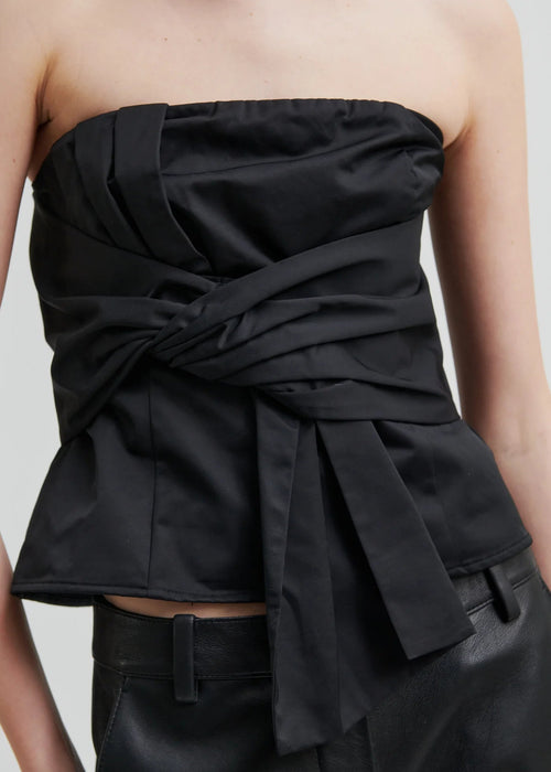 Woman wearing a black strapless top and black pants on a light grey background